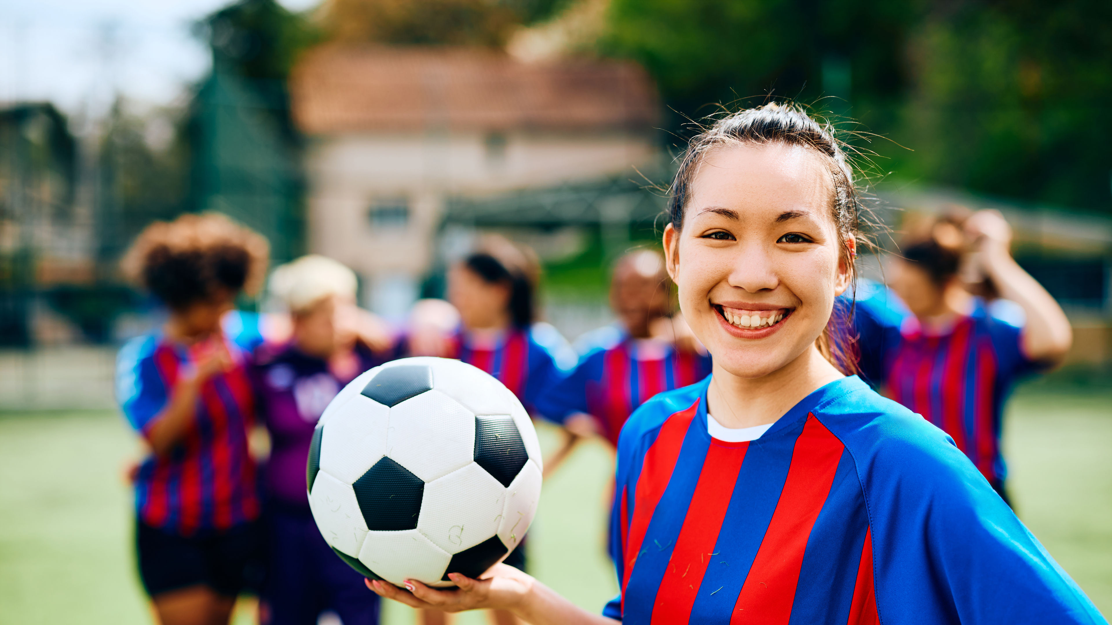 Seorang pemain sepak bola wanita yang bahagia berpose dengan sepak bola di tangan.