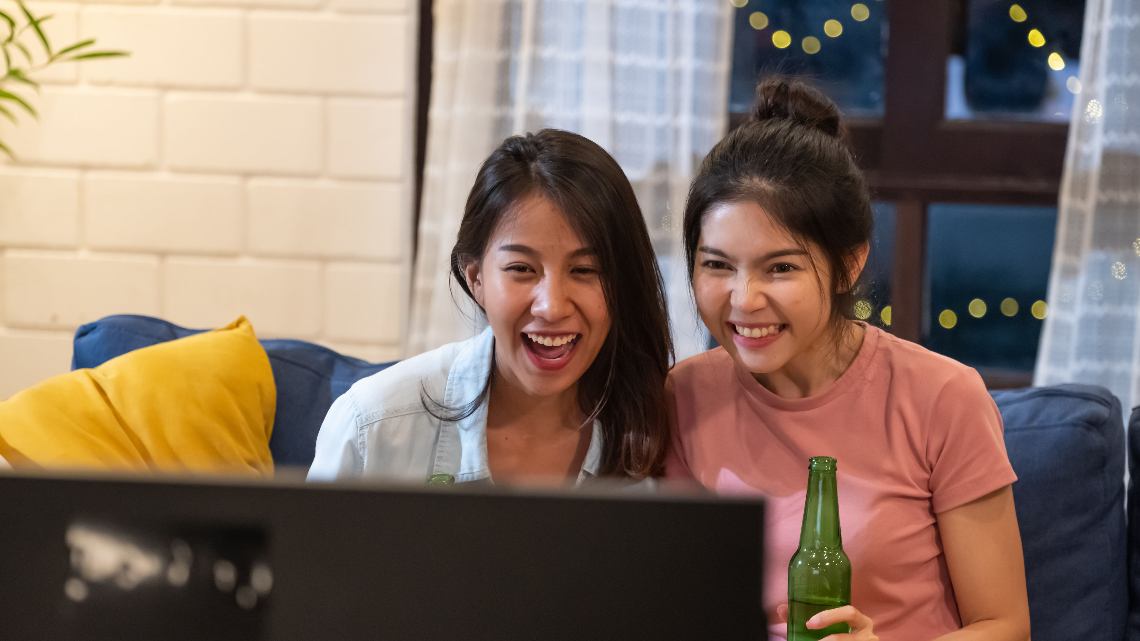 Happy friends cheer football game and celebration with beer on sofa at night at home